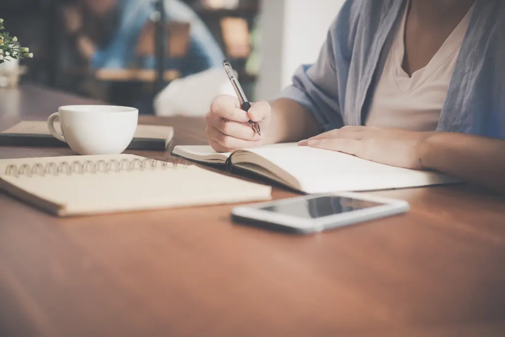 Person writing notes beside a coffee cup